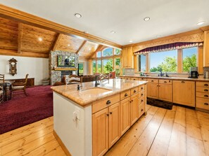 A spacious kitchen with wooden cabinets, a large island, and a stone fireplace. - Luxury View Lodge (Big Bear Lake)