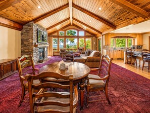 A spacious dining area with a high ceiling and wooden beams, a stone fireplace, and a view of the outdoors. - Luxury View Lodge (Big Bear Lake)
