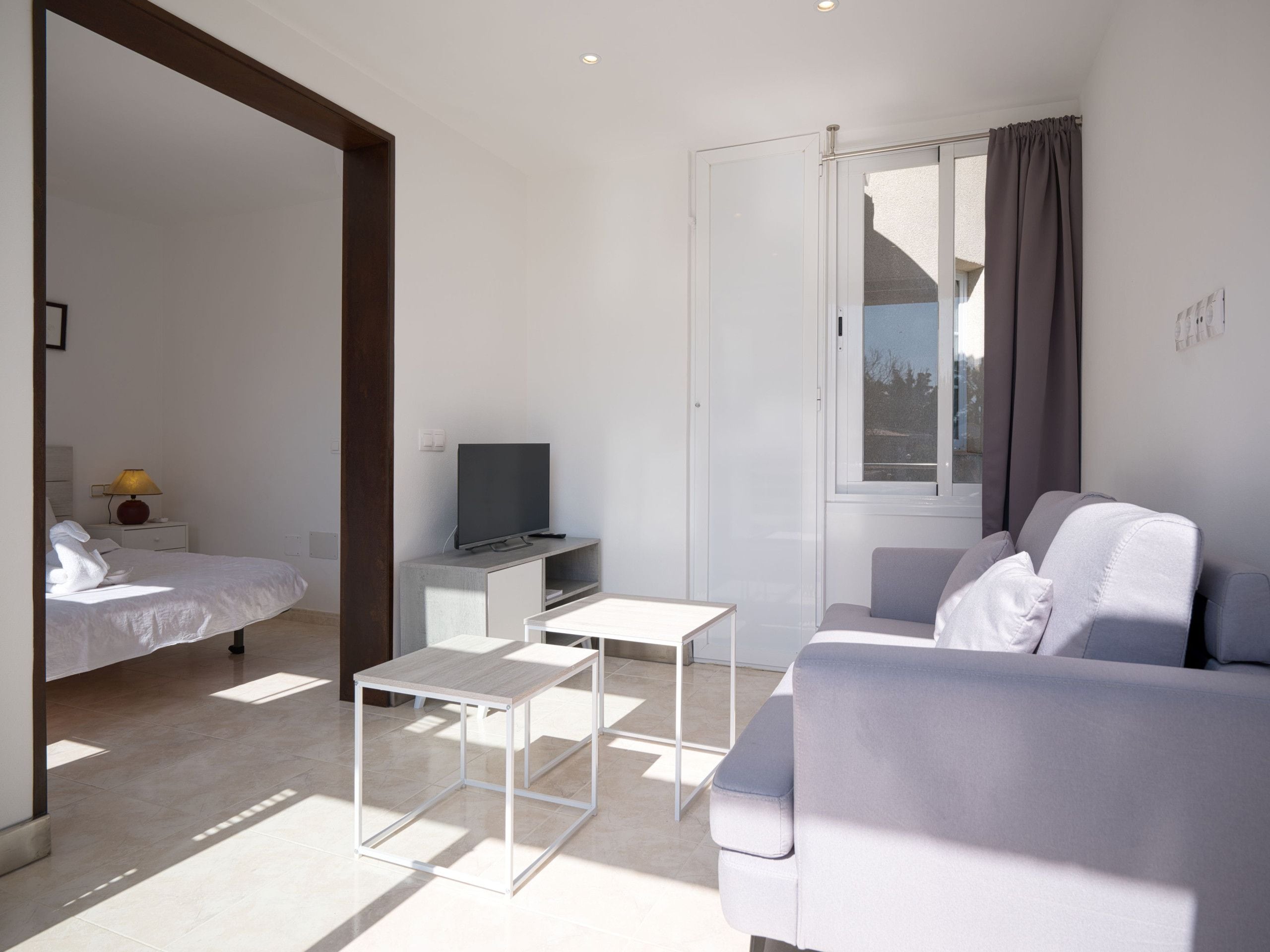 A modern, minimalist bedroom with a bed, bedside table, and a television.