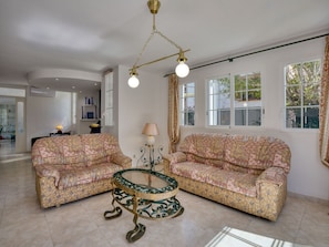 A spacious living room with two patterned sofas, a glass coffee table, and a chandelier.