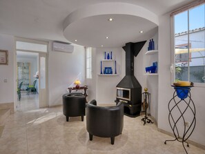 Un salon moderne avec une cheminée, deux fauteuils noirs, une table avec une lampe et des étagères ornées de vases bleus.