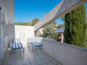 A balcony with two striped lounge chairs, a tiled floor, and a view of trees and buildings.