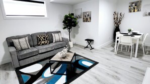 En moderne stue med en grå sofa, et sofabord og et spiseområde med hvide stole og et bord.