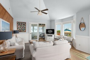 A spacious living room with a ceiling fan, a television, and a view of the outside.