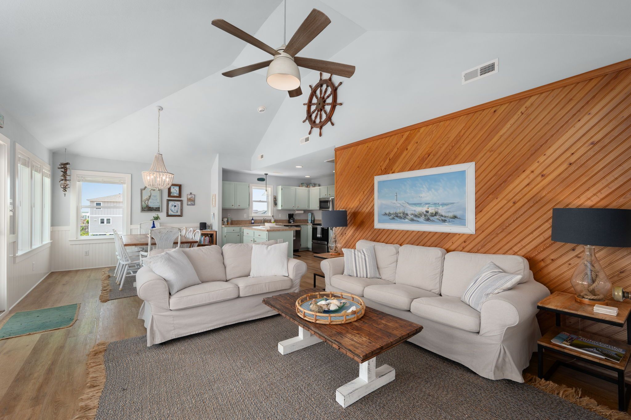 A living room with two sofas, a wooden coffee table, a ceiling fan, and a wooden wall panel.