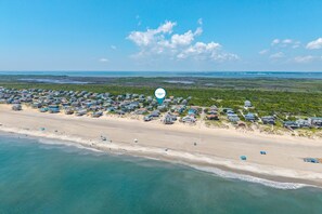 Vue aérienne d’une zone résidentielle côtière, avec des maisons le long de la plage et un ciel dégagé.