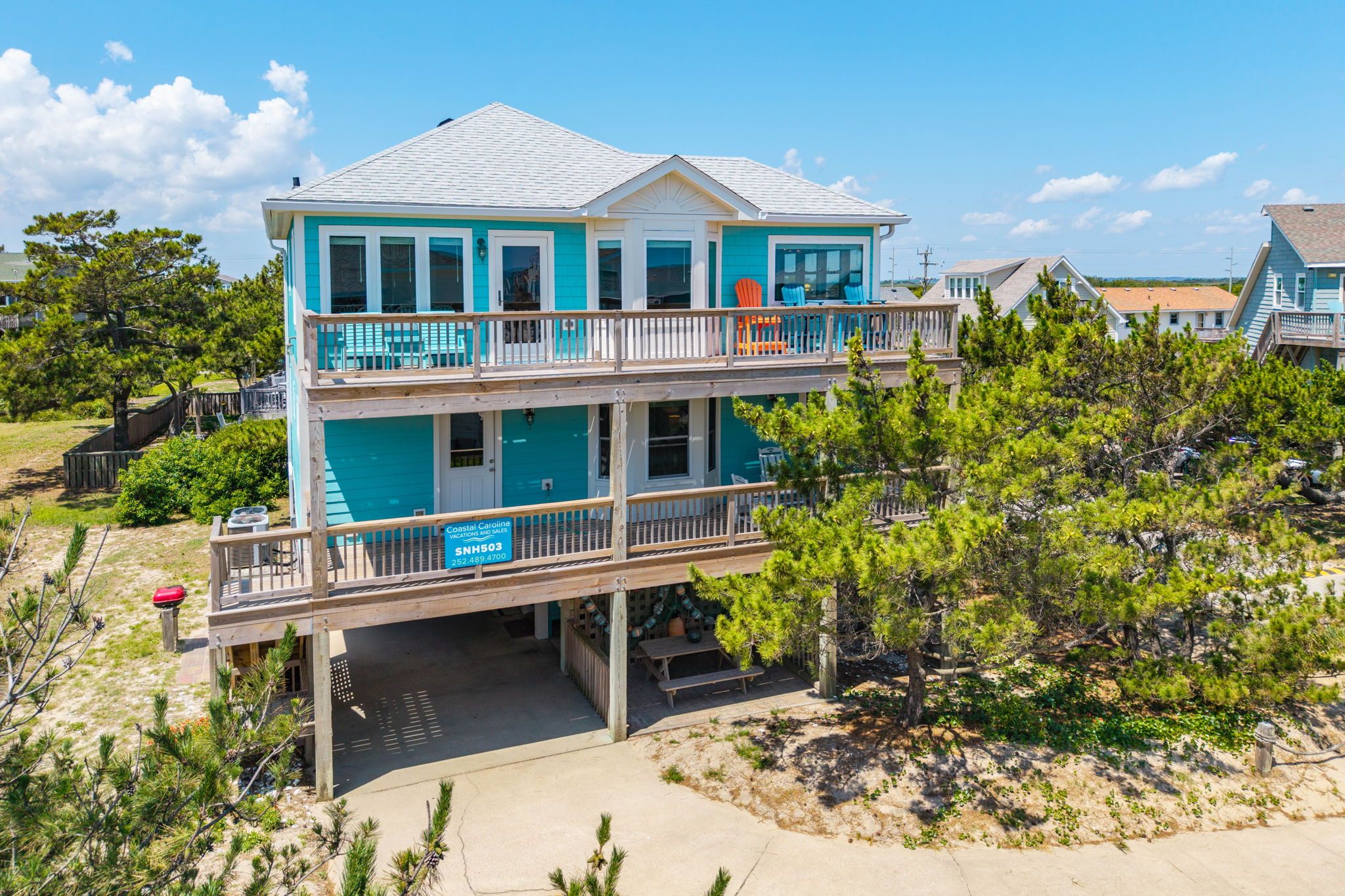 A two-story beachfront house with a balcony, a covered deck, and a sign indicating Coastal Carolina.