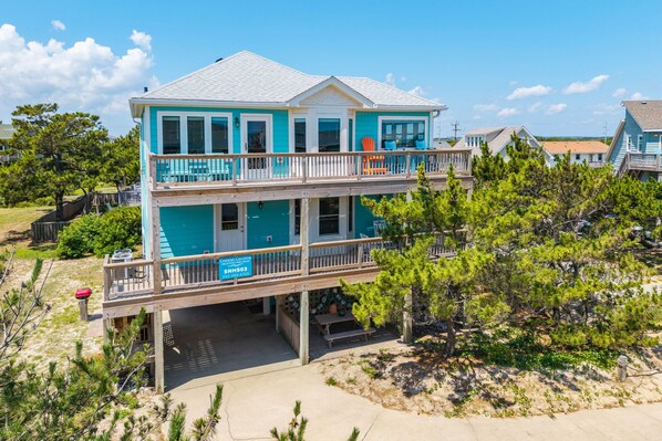 Une maison à deux étages située en bord de mer, dotée d’un balcon, d’une terrasse couverte et d’un panneau indiquant « Coastal Carolina ».