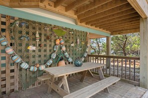 A wooden deck with a picnic table and benches, surrounded by a netted wall decorated with buoys and fish. - Blue Pearl: Steps to the Beach, Ocean Views, Spacious Decks (Nags Head)