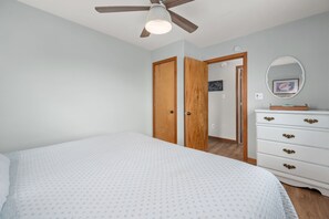 Une chambre à coucher comprenant un lit, une commode, un ventilateur de plafond et une porte donnant sur une autre pièce.