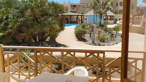 A balcony with a view of a swimming pool, palm trees, and buildings in the background. - Marialva Tropical T2 (Santa Maria)