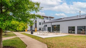 Un bâtiment moderne doté d’un toit plat, de grandes fenêtres et d’une cour dallée avec des tables de pique-nique.