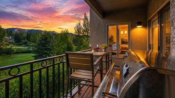 A balcony with a wooden table and chairs, a grill, and a view of a sunset over a mountainous landscape. - The Summit Stay | Pool | Pickleball | Hot Tub (Sun Valley)