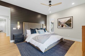 A modern bedroom with a large bed, dark wood paneling, a ceiling fan, and a framed landscape painting. - The Summit Stay | Pool | Pickleball | Hot Tub (Sun Valley)