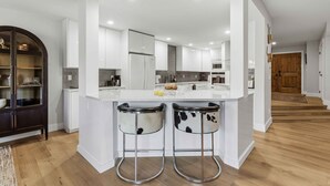 A modern kitchen with white cabinetry, a central island, and two bar stools with cowhide upholstery. - The Summit Stay | Pool | Pickleball | Hot Tub (Sun Valley)