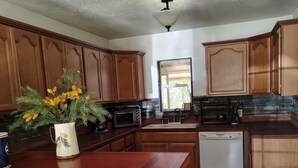 A kitchen with wooden cabinets, a white island with stools, a microwave, a dishwasher, and a window with natural light. - Charming 1-bedroom house in serene Yokuts Valley with WiFi, AC (Yokuts Valley)