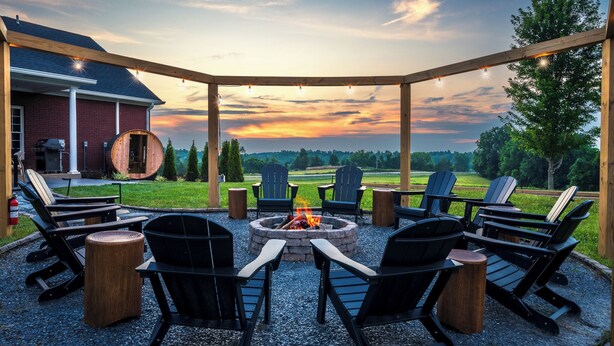 Un espace extérieur aménagé, abrité et doté de chaises Adirondack et d’un foyer, offrant une vue sur un paysage verdoyant.