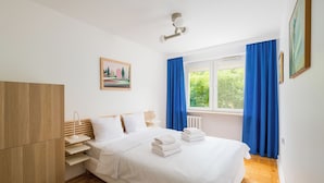 Un dormitorio con cama, armario de madera, mesita de noche, lámpara y ventana con cortinas.