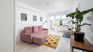 A modern living room with a pink sofa, a patterned rug, a wooden table, and a large potted plant.