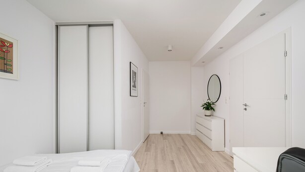 A modern bedroom with a bed, a dresser, a mirror, and a door.