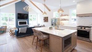 Een moderne keuken met een groot eiland, houten balken, hanglampen en een inbouwoven.