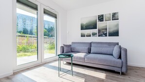 A modern living room with a grey sofa, a small green side table, and a large window offering a view of a residential area.