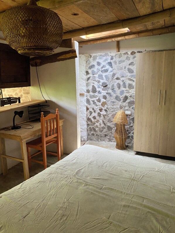 Une chambre à coucher avec un lit en bois, un bureau avec une chaise, une lampe et un mur en pierre.