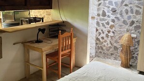 Ein rustikaler Raum mit einem Bett, einem Holztisch, einem Stuhl, einer Hängelampe und einer Steinwand.