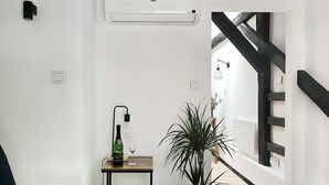 Une chambre à coucher avec un lit, une table de chevet sur laquelle se trouvent une bouteille et un verre, une plante en pot, et une vue sur un escalier.