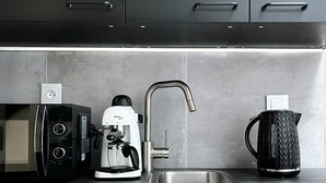 Une cuisine moderne équipée d’un évier en acier inoxydable, d’une machine à café, d’une bouilloire et d’un four à micro-ondes.