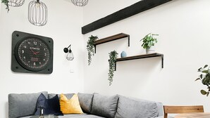 Un salon moderne avec un canapé gris, une table basse en bois, une horloge et des étagères murales ornées de plantes.