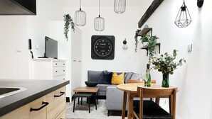 Une cuisine moderne avec des meubles en bois, un plan de travail noir et un four encastré. On y trouve un coin repas avec une table et des chaises en bois, ainsi qu’un canapé gris agrémenté de coussins.