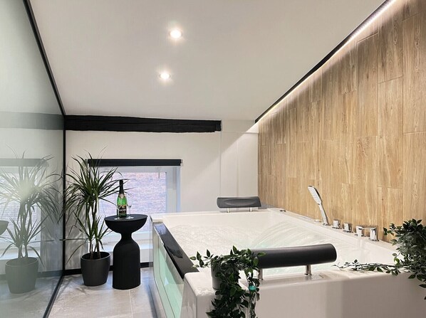 Un baño moderno con una bañera grande, una pared de acento de madera y plantas en macetas.