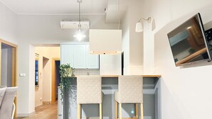 A modern kitchen with two bar stools, a hanging light fixture, and a flat-screen TV mounted on the wall. - Welcoming Apartment with two bedrooms, Świętego Jana (Unknown)