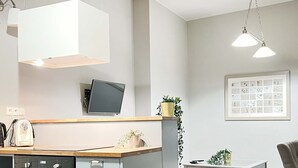 A modern kitchen with a built-in oven, a coffee machine, and a small island with a sink. There is a dining table with chairs and a hanging light fixture above. - Welcoming Apartment with two bedrooms, Świętego Jana (Unknown)
