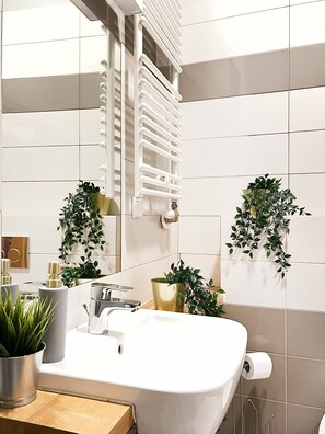 Ein modernes Badezimmer mit einem weißen Waschbecken, einem Spiegel und zwei Blumentöpfen.