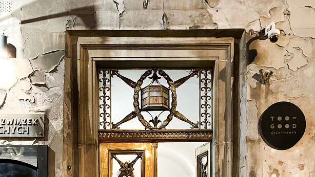 A historic building entrance with ornate golden doors, a security camera, and a sign indicating "TOO-GOOD APARTMENTS." - Welcoming Apartment with two bedrooms, Świętego Jana (Unknown)
