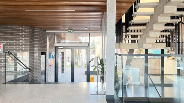 Ein moderner Gebäudeeingang mit Glastür, Holzboden und einer Treppe mit ungewöhnlichem Design.