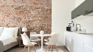 A modern kitchen with white cabinets, a brick wall, and a dining area with a round table and chairs.