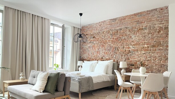 A modern bedroom with a brick wall, a bed, a sofa, a desk, and a chair.