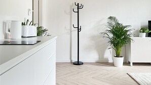 A modern kitchen with white cabinetry, a black coat rack, and a potted plant.