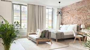 A modern bedroom with a brick wall, a large bed, a sofa, and a dining area.