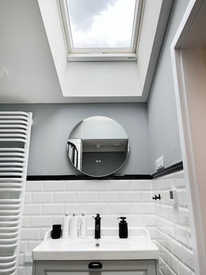 Un bagno moderno con finestra a lucernario, uno specchio rotondo, un lavandino bianco e articoli da toilette.