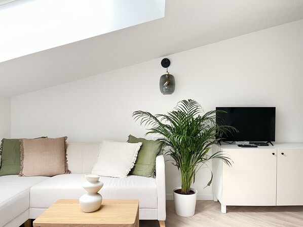 Un soggiorno moderno con un divano bianco, un tavolino, una pianta in vaso, una TV e un mobile.
