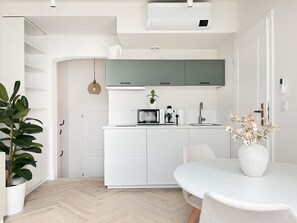 Una cucina moderna con mobili bianchi, forno a microonde integrato, macchina del caffè e lavello. È presente un tavolo da pranzo con sedie e un vaso di fiori.