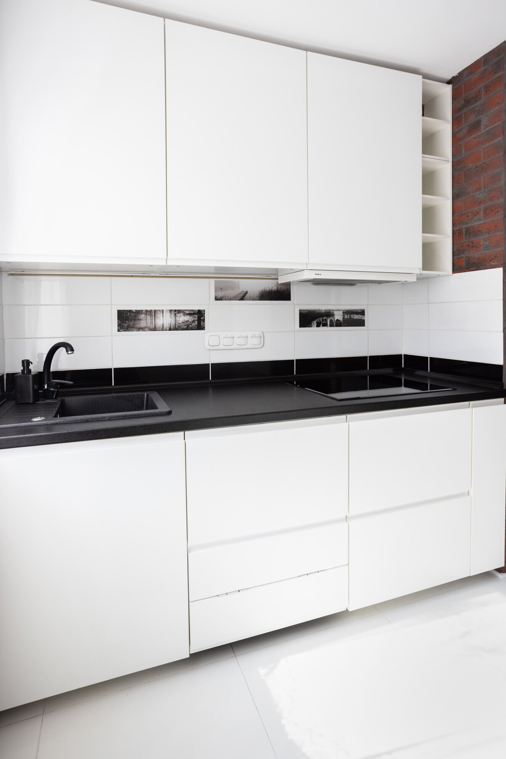 A modern kitchen with white cabinetry, black countertops, and a visible brick wall.