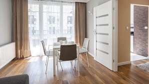 A modern living room with a dining table, chairs, and a view of buildings through sheer curtains.