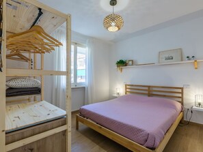A bedroom with a wooden bunk bed, a single bed with a pink bedspread, a hanging light fixture, and a window with curtains. - Casa Rico by Interhome (Cecina)
