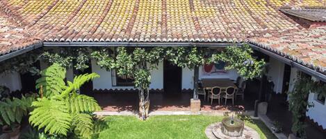 Un patio con techo de tejas, rodeado de follaje y una fuente.