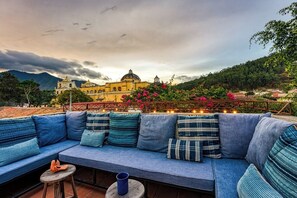 Terraza en la azotea con un sofá azul, una pequeña mesa redonda y vistas a un edificio histórico con cúpulas.